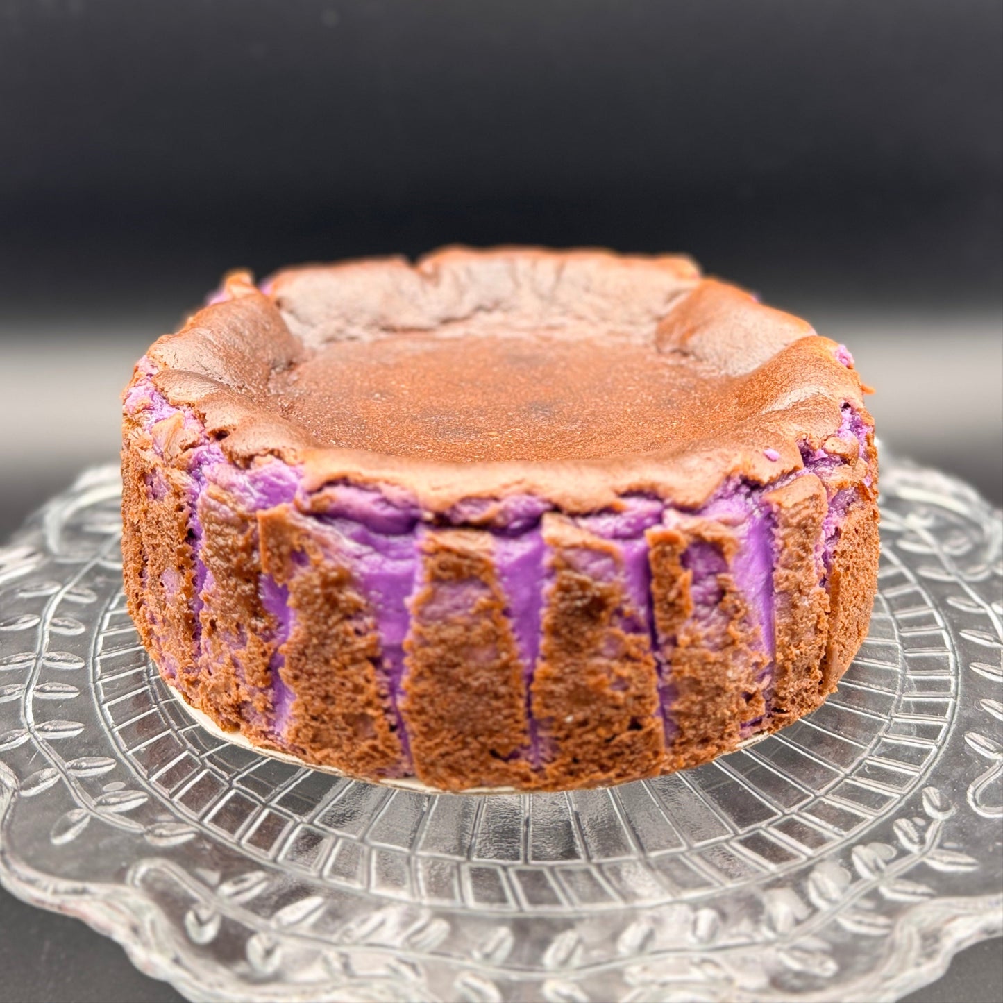 Ube Basque Burnt Cheesecake Gluten Free on a glass plate, showcasing its caramelized top and vibrant purple interior.