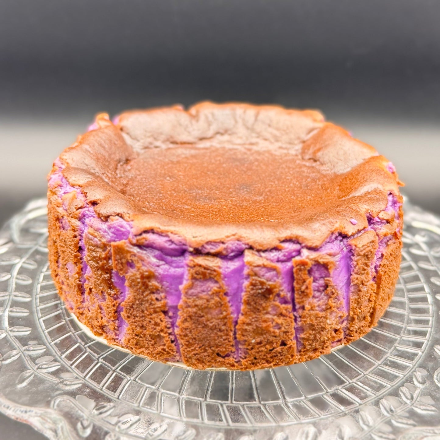 Ube Basque Burnt Cheesecake Gluten Free displayed on a glass plate, showcasing its vibrant purple interior and caramelized top.