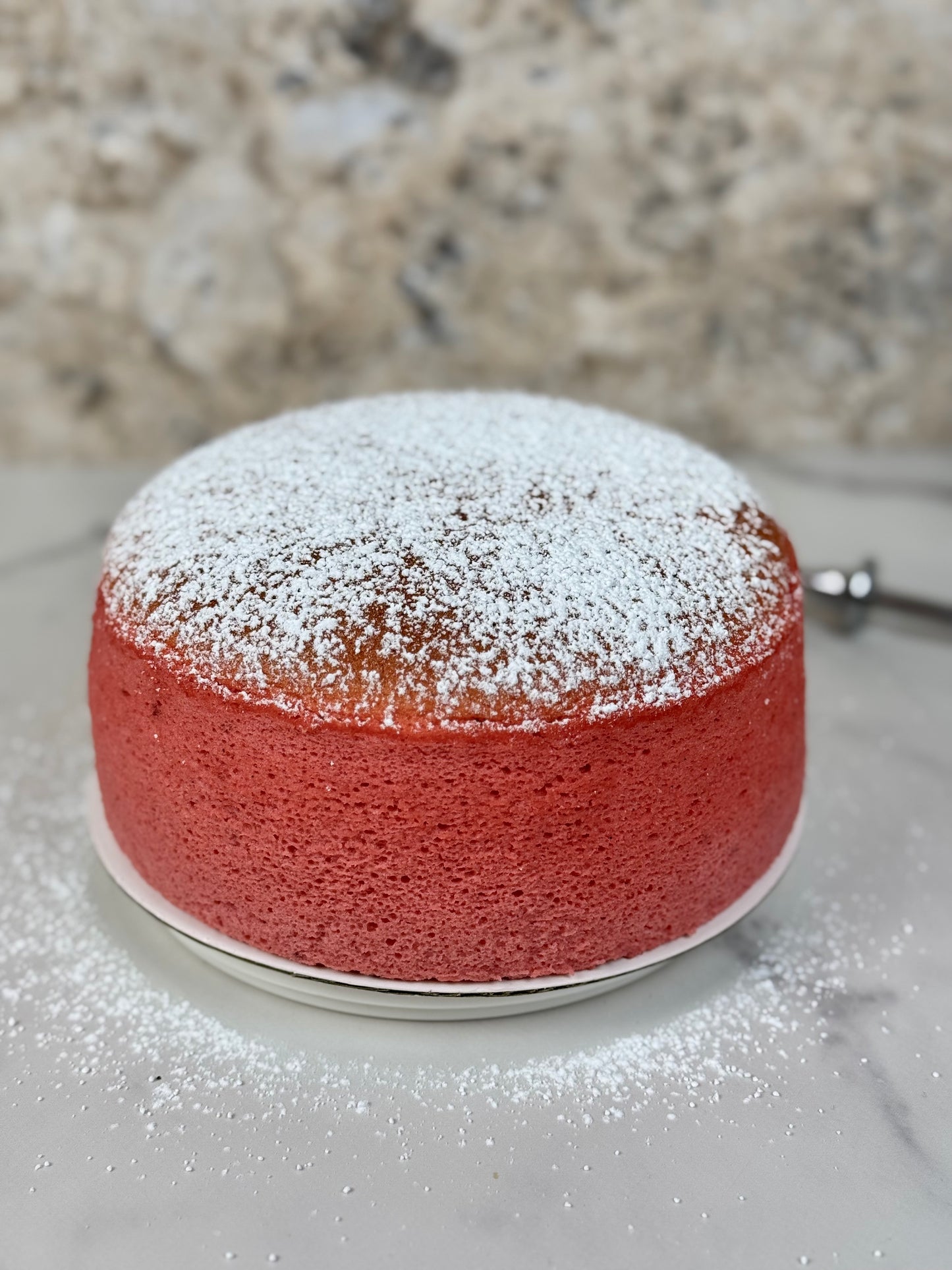 Strawberry Japanese souffle cheesecake dusted with powdered sugar on a marble countertop.