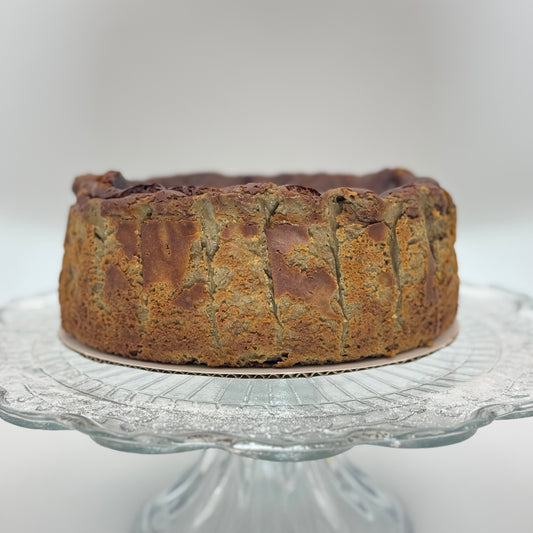 Organic Hojicha Burnt Basque Cheesecake displayed on a glass cake stand, showcasing its caramelized top.