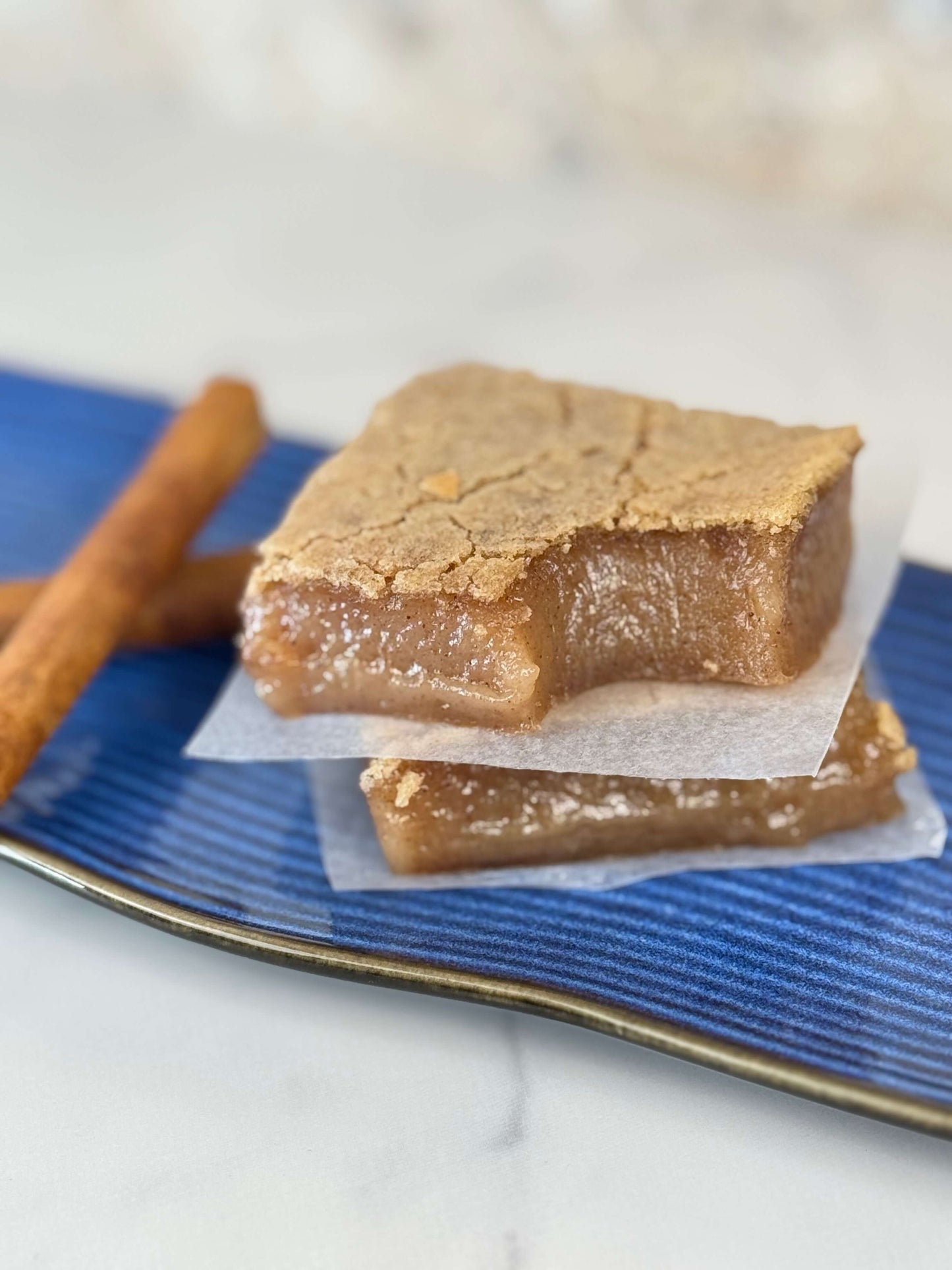 Vegan cinnamon maple butter mochi on a blue plate with cinnamon sticks, soft and chewy organic treat.
