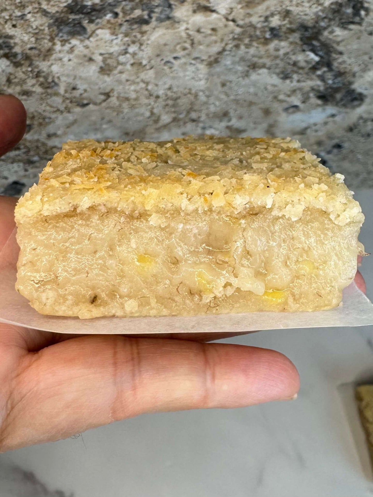 Vegan Banana Mochi Cake Bar Organic Sugar Free holding in hand, showcasing its soft texture and golden topping.
