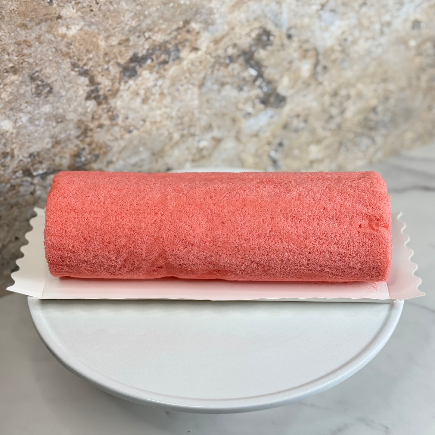 Rose Strawberry Cake Roll on a white plate, showcasing its vibrant pink color and fluffy texture.