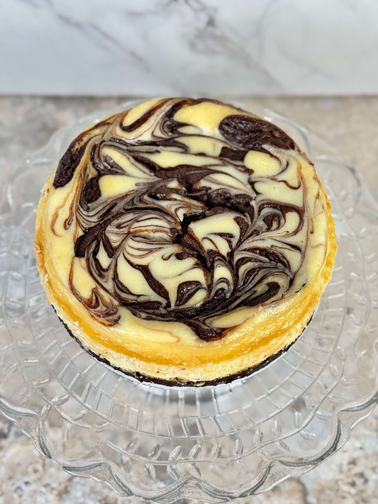 Swirl brownie cheesecake with chocolate swirl on a glass cake stand.