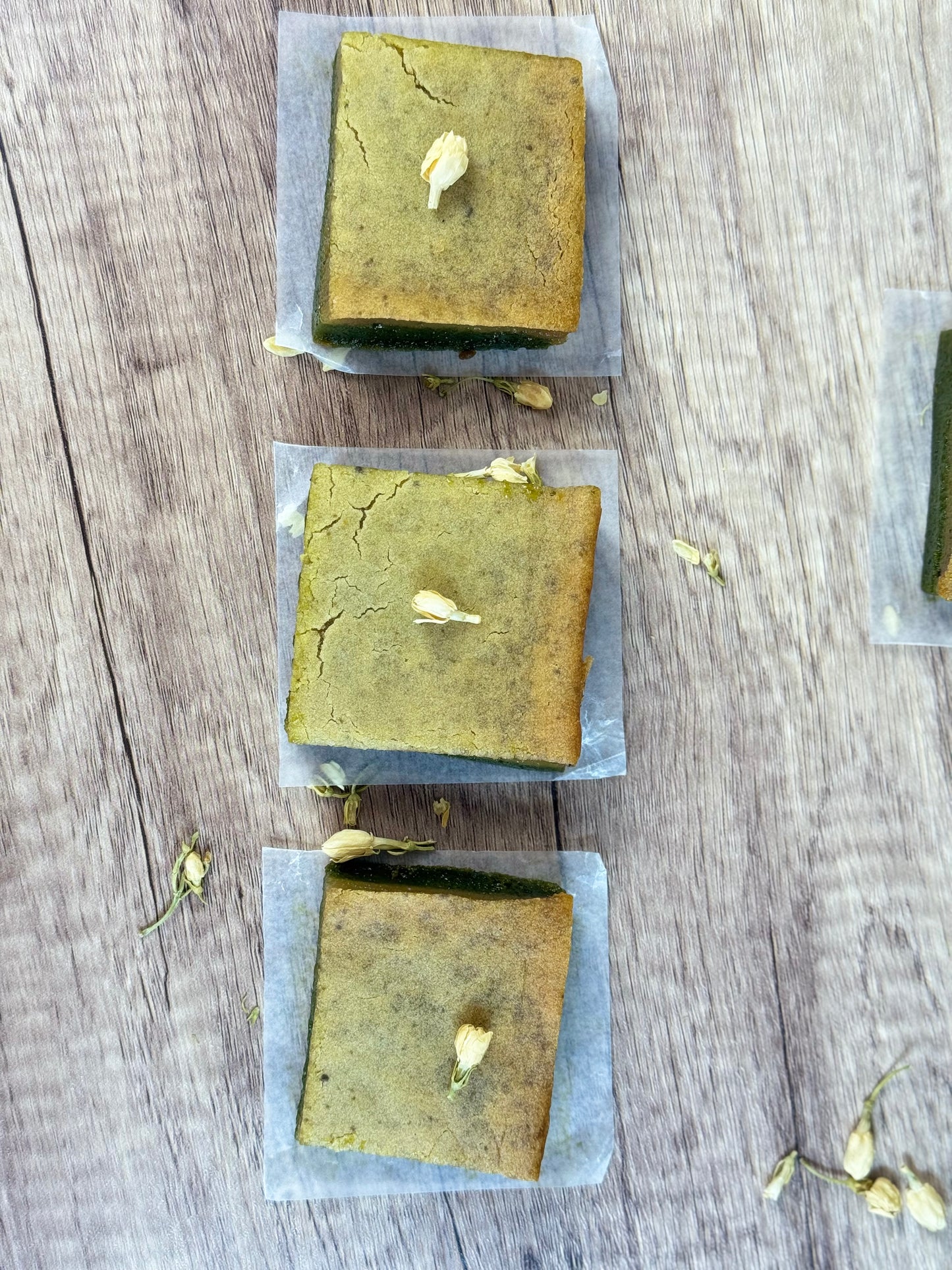 Vegan Jasmine Matcha Mochi Cake, organic dessert, squares on parchment with jasmine flowers, plant-based treat.