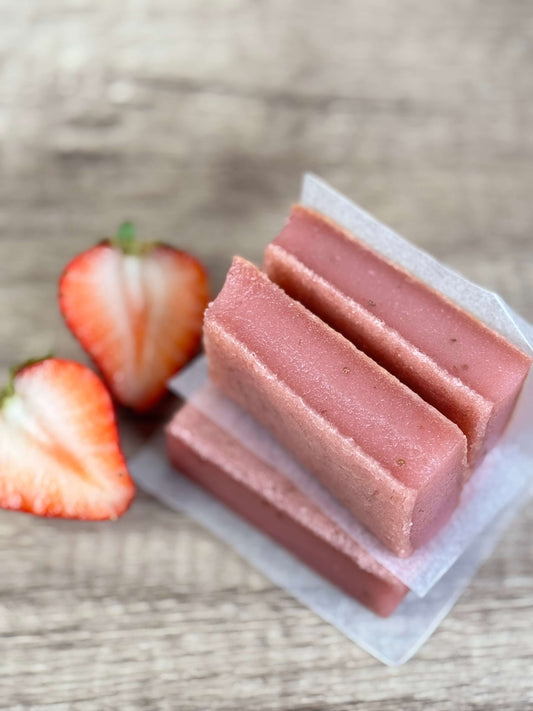 Vegan Strawberry Mochi Cake Bars stacked on parchment paper with fresh strawberries, highlighting their chewy texture.