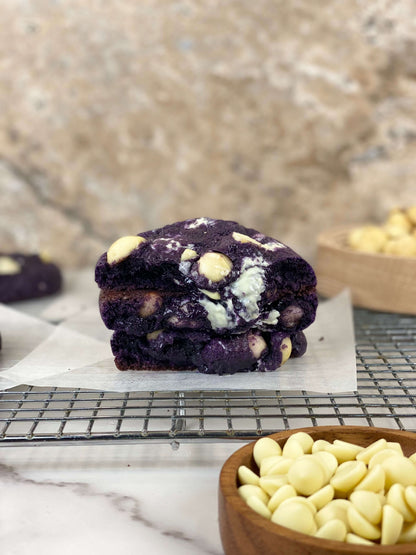 Ube White Chocolate Macadamia Cookies stacked on a cooling rack with white chocolate chips in the foreground.