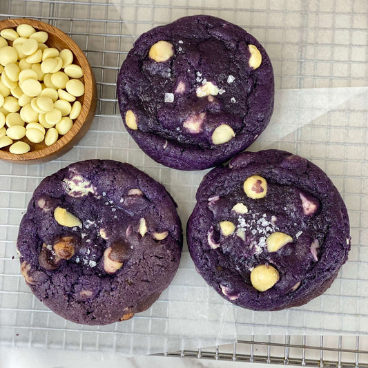 Ube White Chocolate Macadamia Cookies with creamy white chocolate chunks and macadamia nuts on a baking rack.