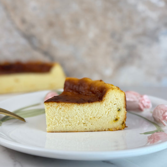 Gluten free passion fruit burnt cheesecake slice on a plate with light pink flowers and a fork.