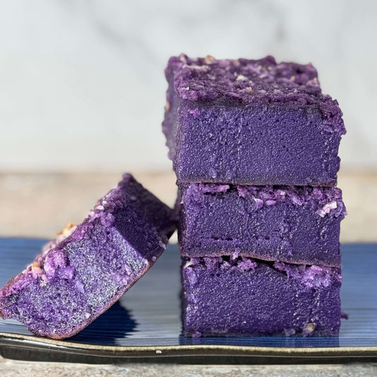 Ube Coconut Butter Mochi Cake Bars stacked on a blue plate, showcasing their vibrant purple color and creamy texture.