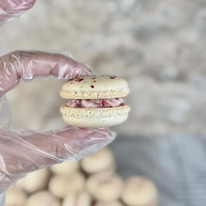 Organic rose macaron held in hand with pink filling and almond shell, showcasing delicate French confection.