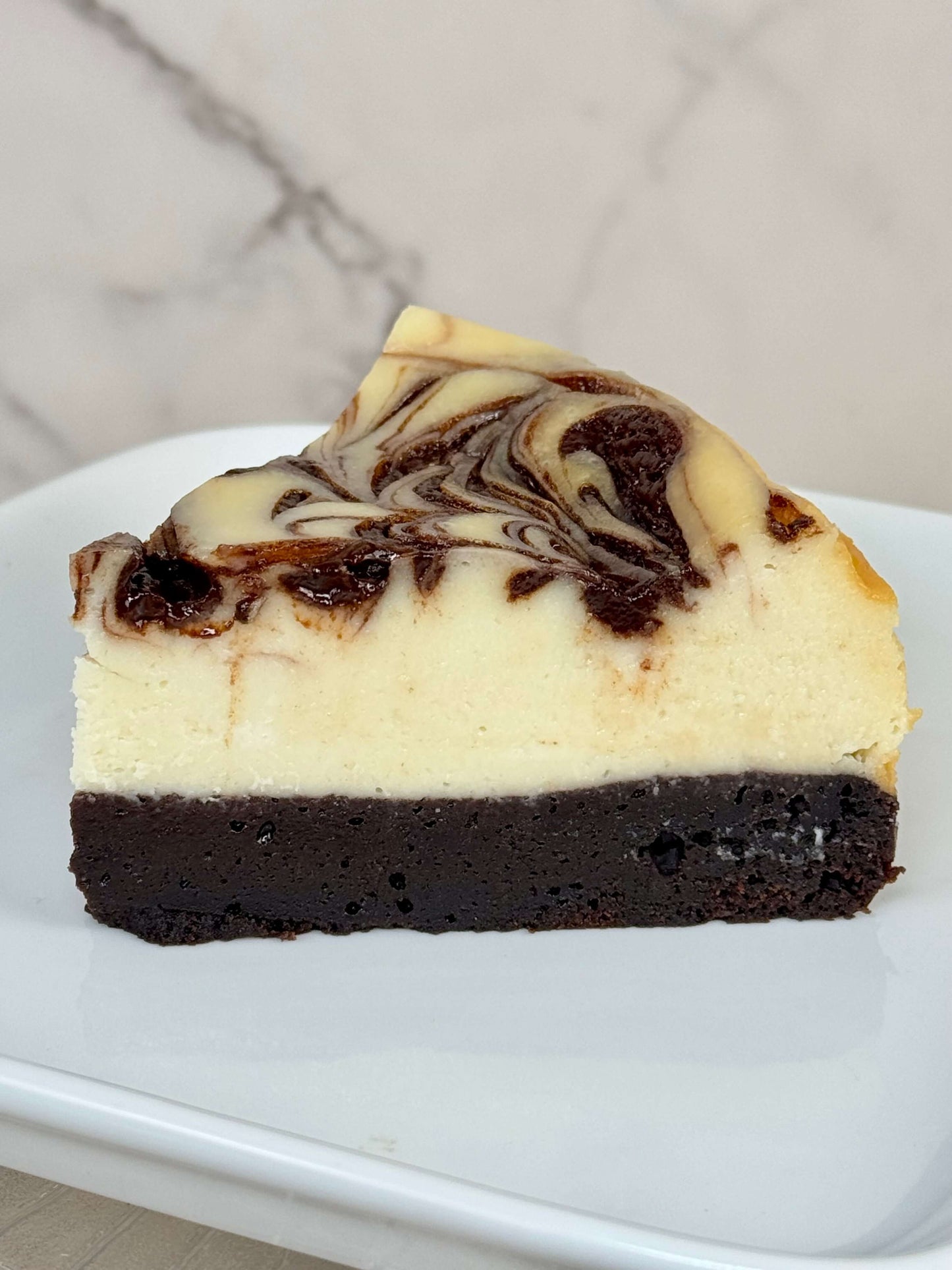 Swirl brownie cheesecake slice with chocolate swirl on top and fudgy brownie base.