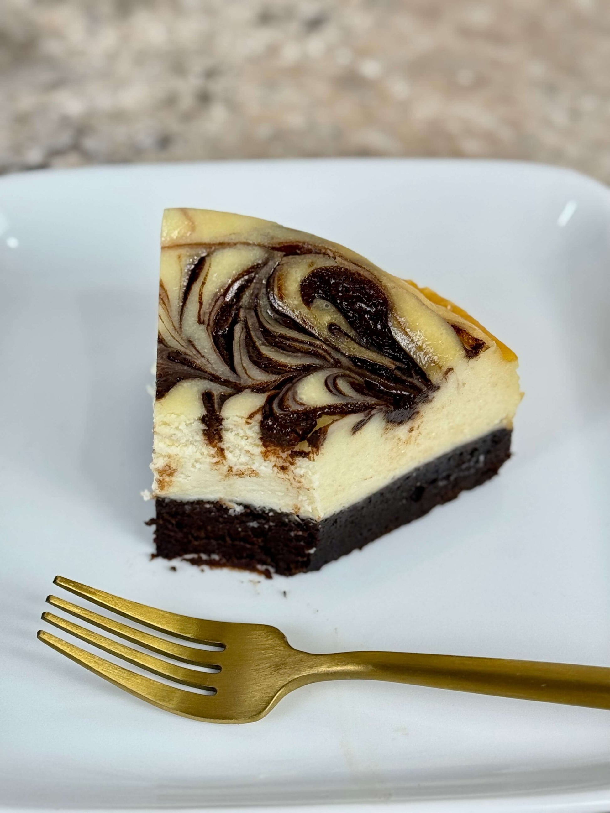 Swirl brownie cheesecake slice on a plate with a golden fork beside it.
