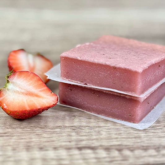 Vegan Strawberry Mochi Cake Bars stacked with fresh strawberries on a wooden surface.